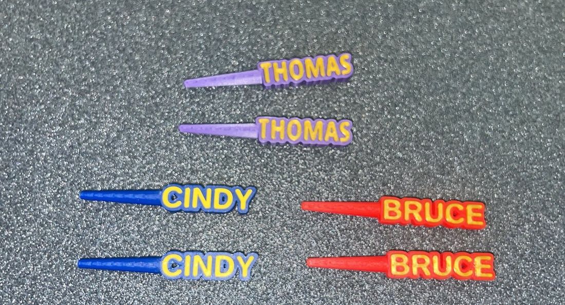 Custom 29 Club cribbage pegs in purple, blue and red with gold lettering reading THOMAS, CINDY and BRUCE